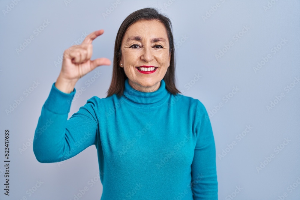 Middle age hispanic woman standing over isolated background smiling and confident gesturing with hand doing small size sign with fingers looking and the camera. measure concept. Middle age hispanic woman standing over isolated background smiling and confident gesturing with hand doing small size sign with fingers looking and the camera. measure concept.