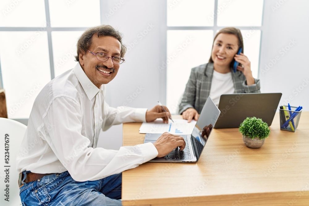 Middle age man and woman business workers using laptop and talking on the smartphone at office Middle age man and woman business workers using laptop and talking on the smartphone at office