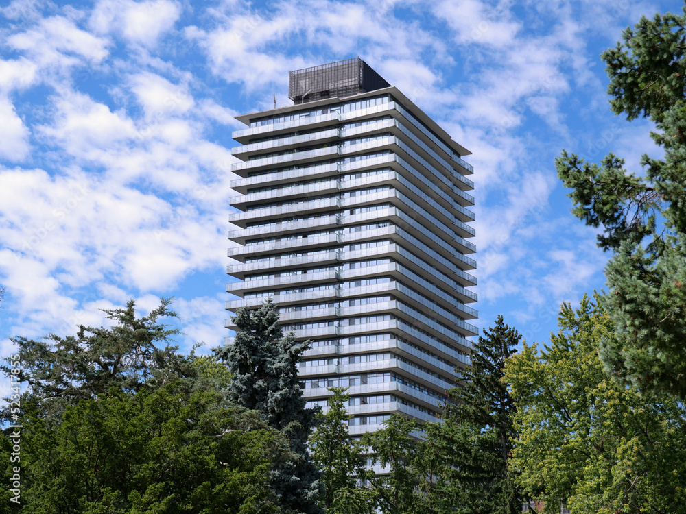 Tall modern apartment building with balconies, surrounded by trees