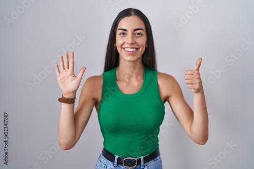 Young woman standing over isolated background showing and pointing up with fingers number six while smiling confident and happy.