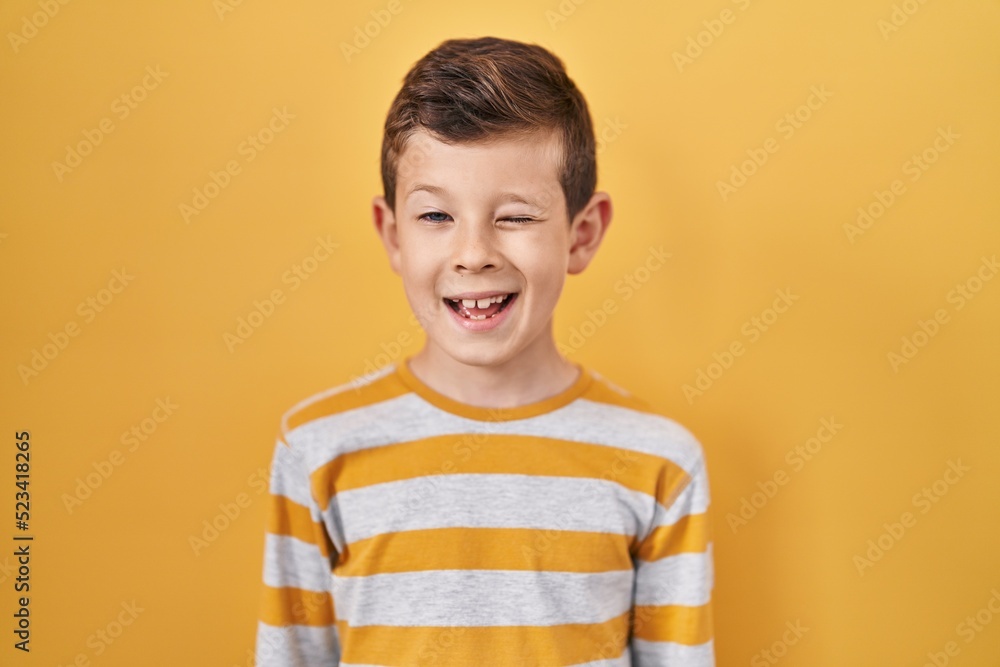 Young caucasian kid standing over yellow background winking looking at the camera with sexy expression, cheerful and happy face. Young caucasian kid standing over yellow background winking looking at the camera with sexy expression, cheerful and happy face.