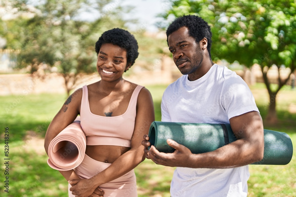 African american man and woman couple holding yoga mat standing together at park African american man and woman couple holding yoga mat standing together at park