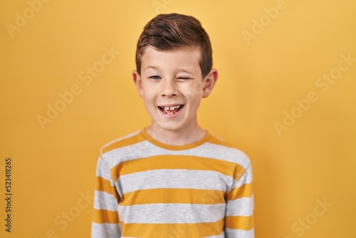 Young caucasian kid standing over yellow background winking looking at the camera with sexy expression, cheerful and happy face.