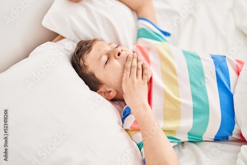 Blond child waking up lying on bed at bedroom