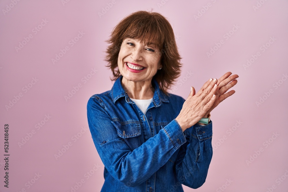 Middle age woman standing over pink background clapping and applauding happy and joyful, smiling proud hands together Middle age woman standing over pink background clapping and applauding happy and joyful, smiling proud hands together