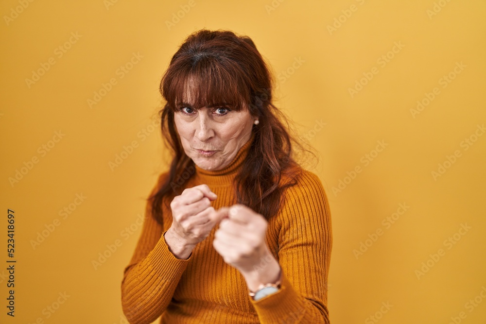 Middle age hispanic woman standing over yellow background ready to fight with fist defense gesture, angry and upset face, afraid of problem Middle age hispanic woman standing over yellow background ready to fight with fist defense gesture, angry and upset face, afraid of problem