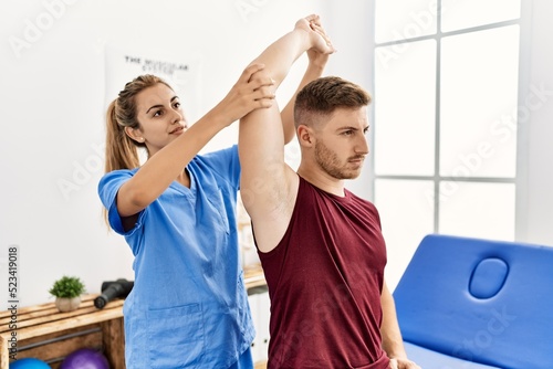 Young hispanic physioterapist woman make arm rehab treatment to man at the clinic. photo