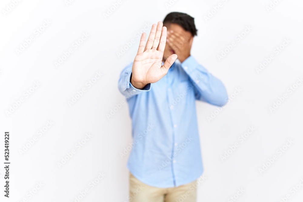 Young hispanic man wearing business shirt standing over isolated background covering eyes with hands and doing stop gesture with sad and fear expression. embarrassed and negative concept. Young hispanic man wearing business shirt standing over isolated background covering eyes with hands and doing stop gesture with sad and fear expression. embarrassed and negative concept.