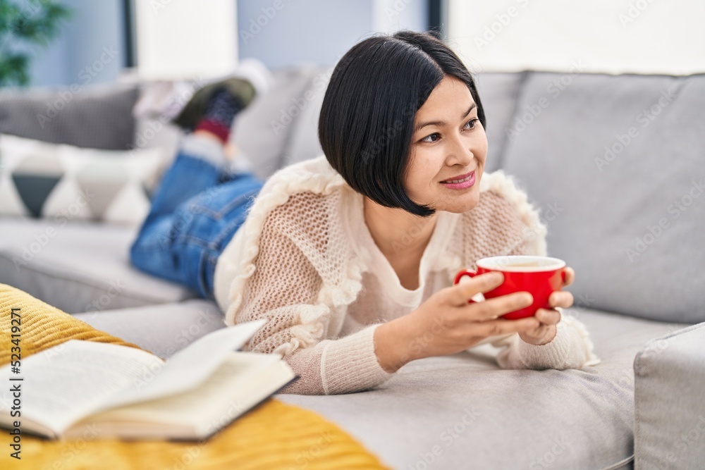 Young chinese woman drinking coffee lying on sofa at home Young chinese woman drinking coffee lying on sofa at home
