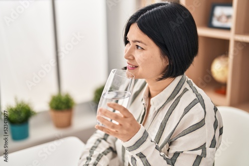 Young chinese woman drinking water sitting on table at home