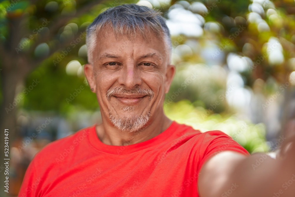 Middle age grey-haired man smiling confident making selfie by camera at park Middle age grey-haired man smiling confident making selfie by camera at park