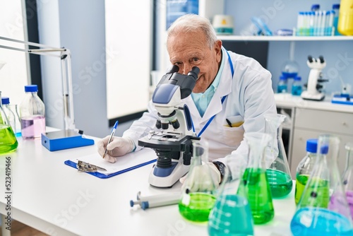 Senior man wearing scientist uniform using microscope at laboratory