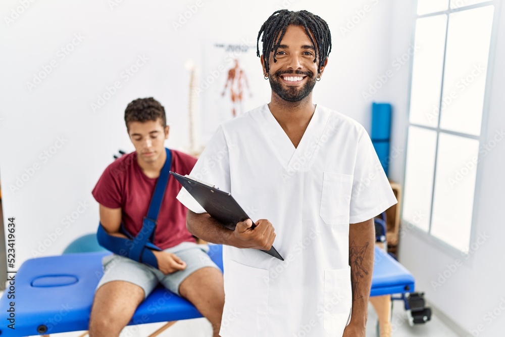 Fototapeta premium Young hispanic man working at pain recovery clinic with a man with broken arm with a happy and cool smile on face. lucky person.