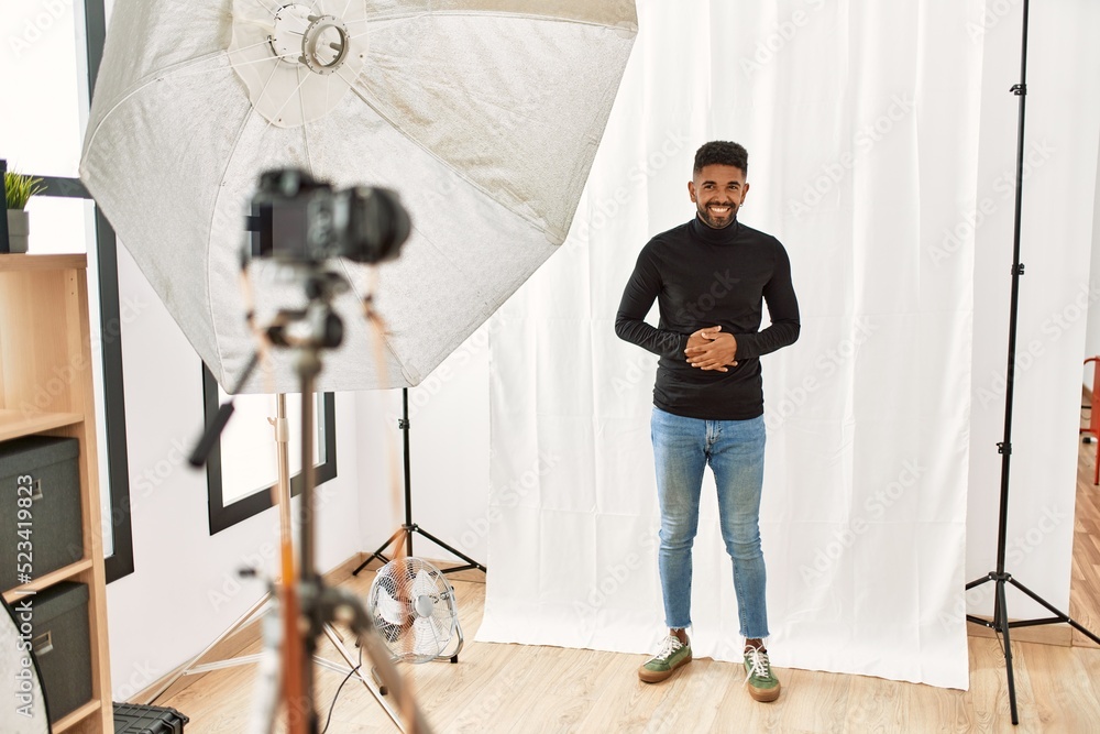 Young hispanic man with beard posing as model at photography studio with hand on stomach because nausea, painful disease feeling unwell. ache concept.