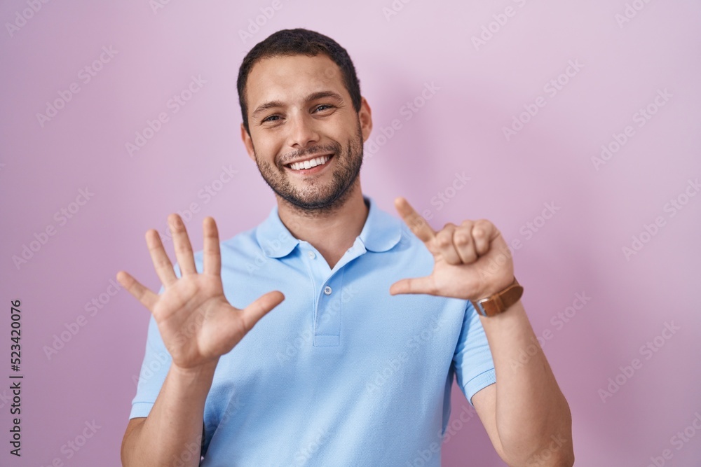Hispanic man standing over pink background showing and pointing up with fingers number seven while smiling confident and happy. Hispanic man standing over pink background showing and pointing up with fingers number seven while smiling confident and happy.