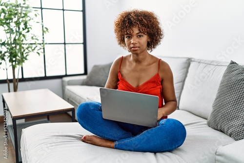 Young african american woman sitting on the sofa at home using laptop relaxed with serious expression on face. simple and natural looking at the camera.