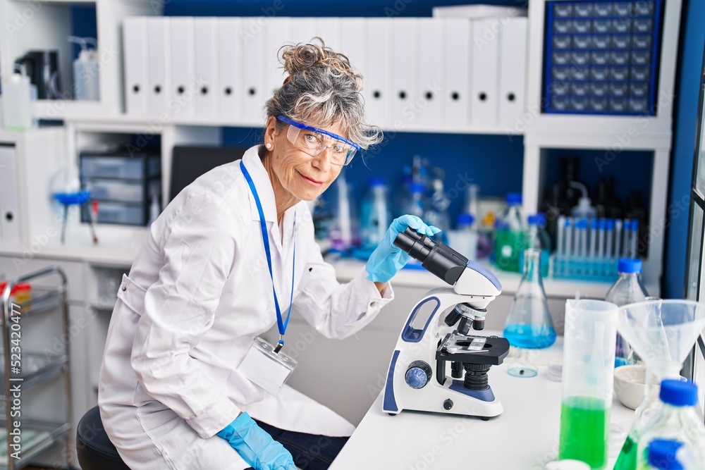 Middle age woman scientist using microscope working at laboratory