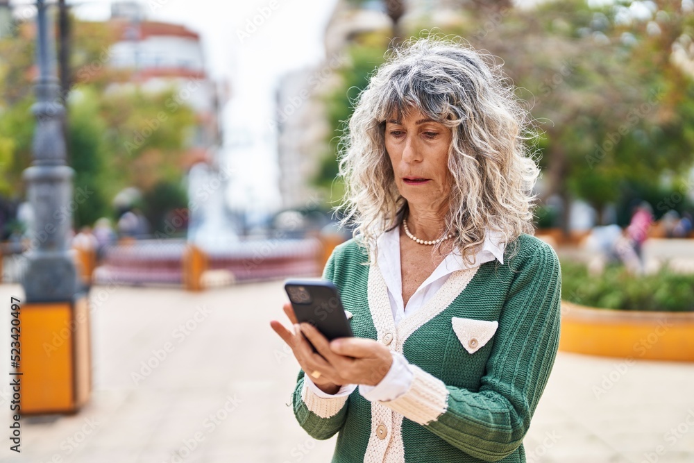 Fototapeta premium Middle age woman using smartphone at park