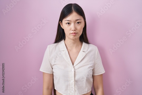Chinese young woman standing over pink background relaxed with serious expression on face. simple and natural looking at the camera. © Krakenimages.com
