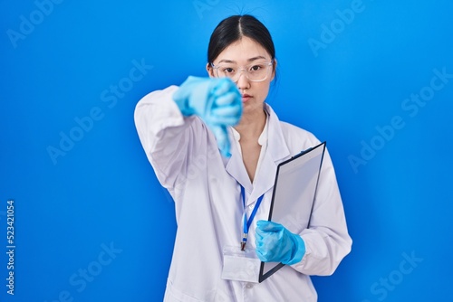 Chinese young woman working at scientist laboratory looking unhappy and angry showing rejection and negative with thumbs down gesture. bad expression.