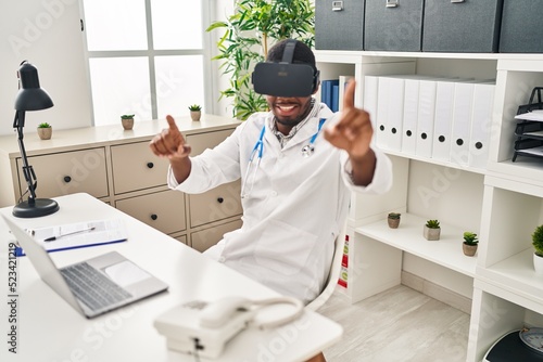 Young african american man wearing doctor uniform using virtual reality glasses at clinic
