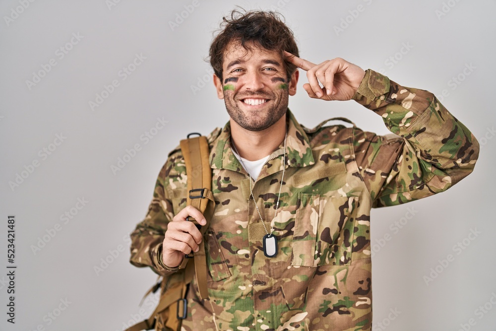 Hispanic young man wearing camouflage army uniform smiling pointing to head with one finger, great idea or thought, good memory