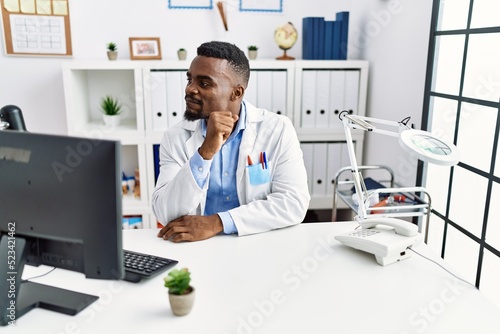 Young african doctor man wearing stethoscope at the clinic looking to side  relax profile pose with natural face with confident smile.