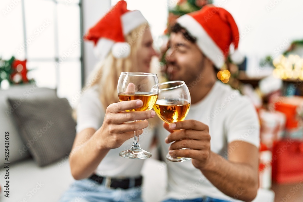 Young couple smiling happy wearing christmas hat toasting with champagne at home