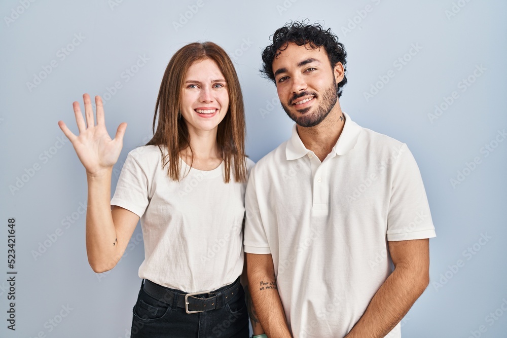 Young couple wearing casual clothes standing together showing and pointing up with fingers number five while smiling confident and happy. Young couple wearing casual clothes standing together showing and pointing up with fingers number five while smiling confident and happy.