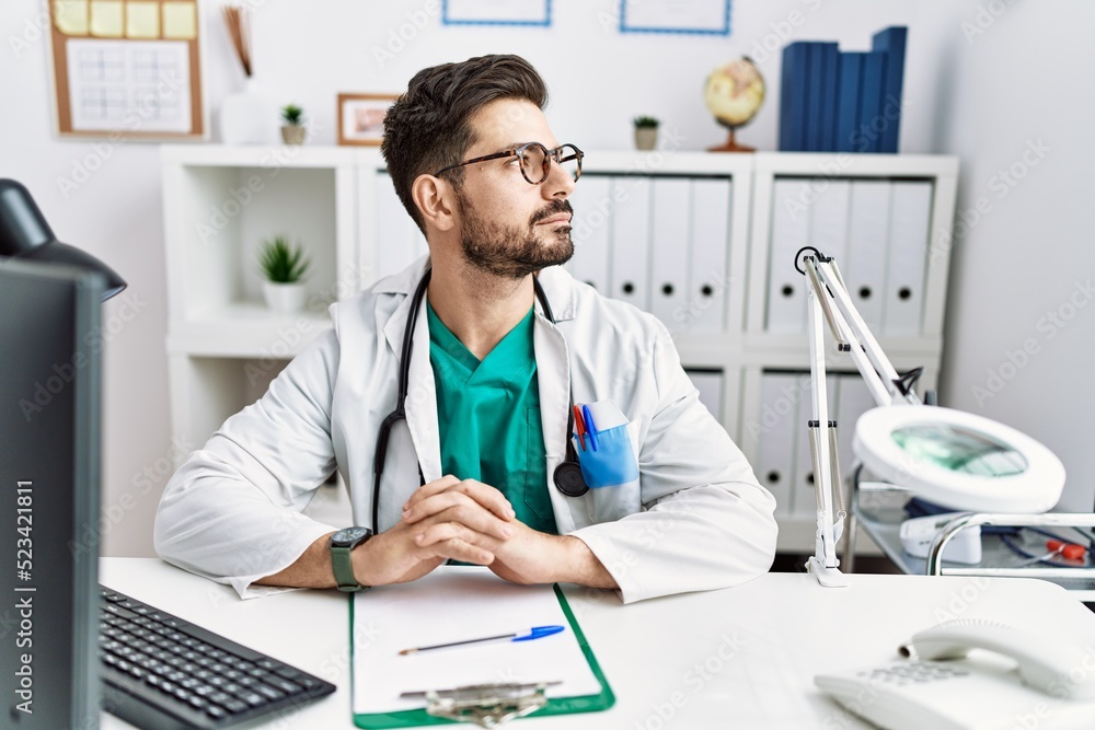 Young man with beard wearing doctor uniform and stethoscope at the clinic looking to side, relax profile pose with natural face and confident smile. Young man with beard wearing doctor uniform and stethoscope at the clinic looking to side, relax profile pose with natural face and confident smile.
