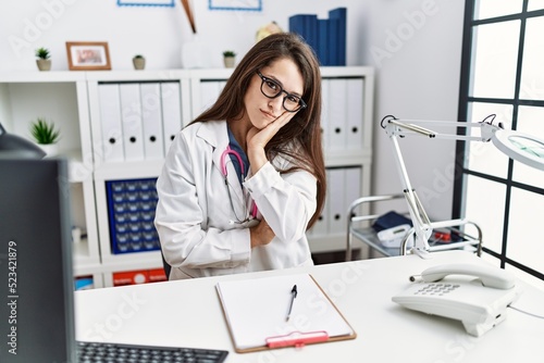 Young doctor woman wearing doctor uniform and stethoscope at the clinic thinking looking tired and bored with depression problems with crossed arms.