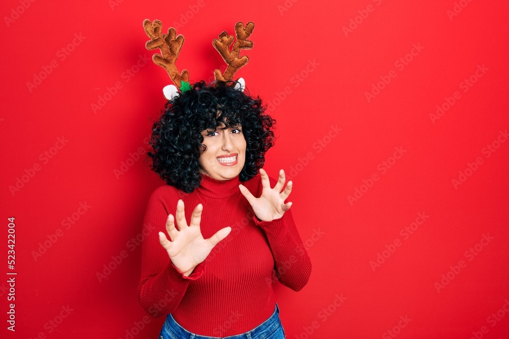 Young middle east woman wearing cute christmas reindeer horns disgusted expression, displeased and fearful doing disgust face because aversion reaction. with hands raised Young middle east woman wearing cute christmas reindeer horns disgusted expression, displeased and fearful doing disgust face because aversion reaction. with hands raised
