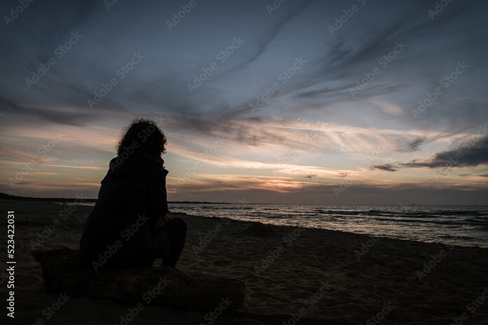 Silhouette of a woman watching the sunset on the beach by the Baltic Sea