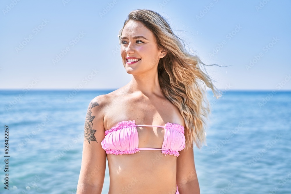 Young blonde girl wearing bikini standing at the beach.