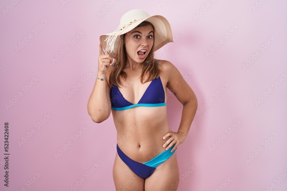 Young hispanic woman wearing bikini over pink background pointing finger up with successful idea. exited and happy. number one. Young hispanic woman wearing bikini over pink background pointing finger up with successful idea. exited and happy. number one.