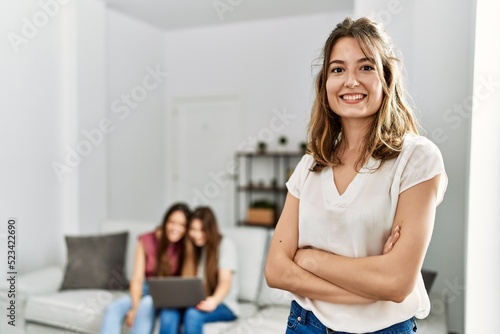 Woman smiling happy standing with arms crossed gesture while friends using laptop at home.
