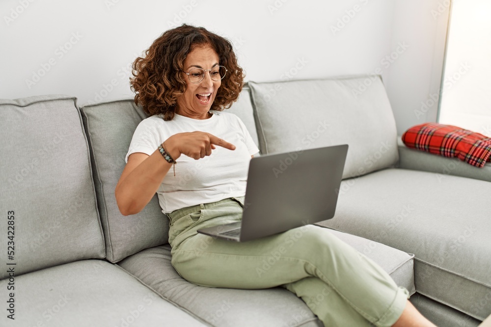 Middle age hispanic woman working using computer laptop at home smiling happy pointing with hand and finger Middle age hispanic woman working using computer laptop at home smiling happy pointing with hand and finger