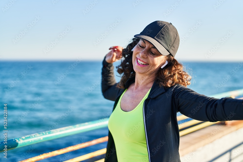Middle age hispanic woman working out listening music with earphones dancing at promenade