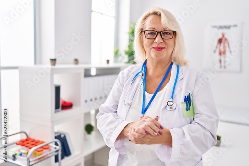 Middle age blonde woman wearing doctor uniform standing at clinic