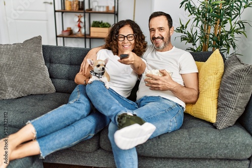 Middle age hispanic couple watching movie and eating popcorn sitting on the sofa at home.