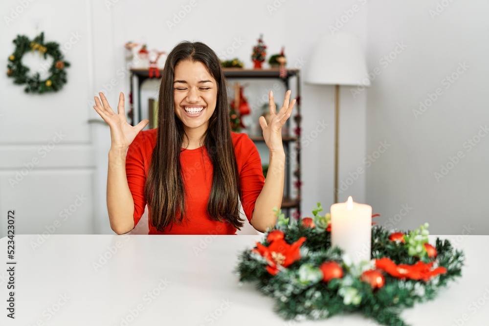 Young brunette woman sitting on the table on christmas celebrating mad and crazy for success with arms raised and closed eyes screaming excited. winner concept Young brunette woman sitting on the table on christmas celebrating mad and crazy for success with arms raised and closed eyes screaming excited. winner concept