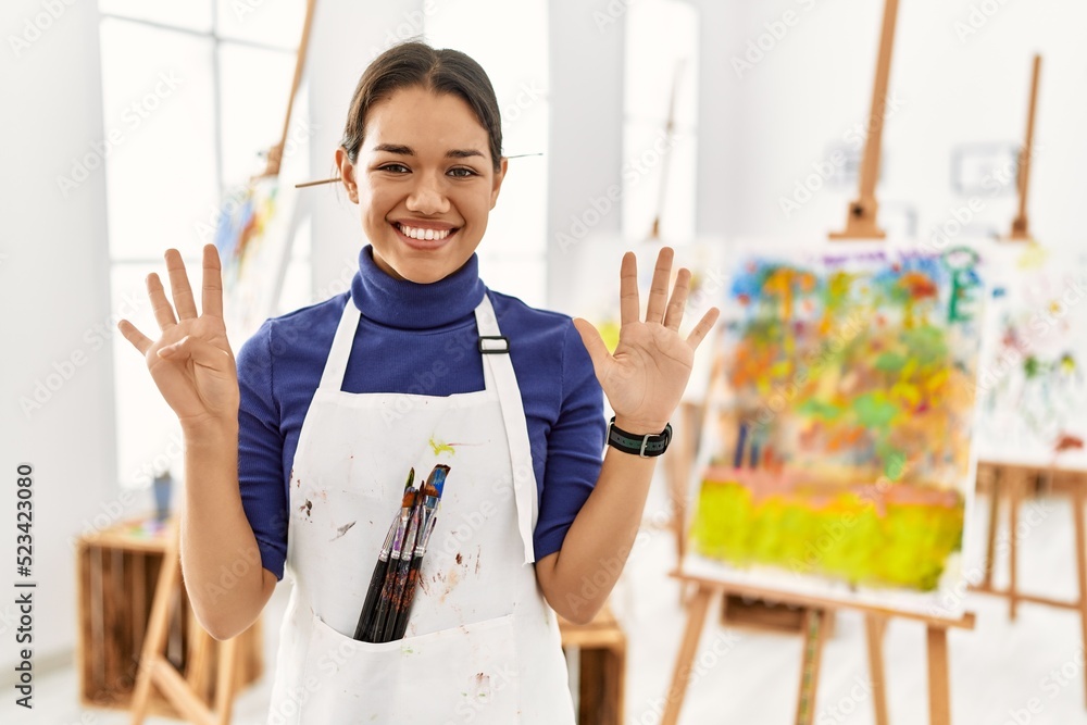 © Krakenimages.com - Young brunette woman at art studio showing and pointing up with fingers number nine while smiling confident and happy. © Krakenimages.com - Young brunette woman at art studio showing and pointing up with fingers number nine while smiling confident and happy.