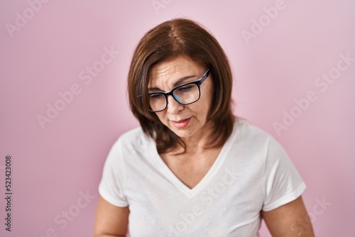 Middle age hispanic woman standing over pink background with hand on stomach because indigestion, painful illness feeling unwell. ache concept.