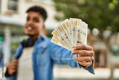 Hispanic young man holding 100 danish krone baknotes at the street photo