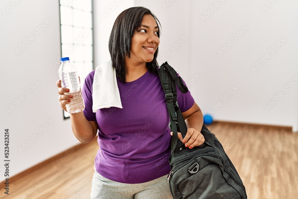 Hispanic brunette woman wearing sportwears holding water at gym room Hispanic brunette woman wearing sportwears holding water at gym room