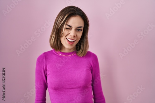 Hispanic woman standing over pink background winking looking at the camera with sexy expression  cheerful and happy face.