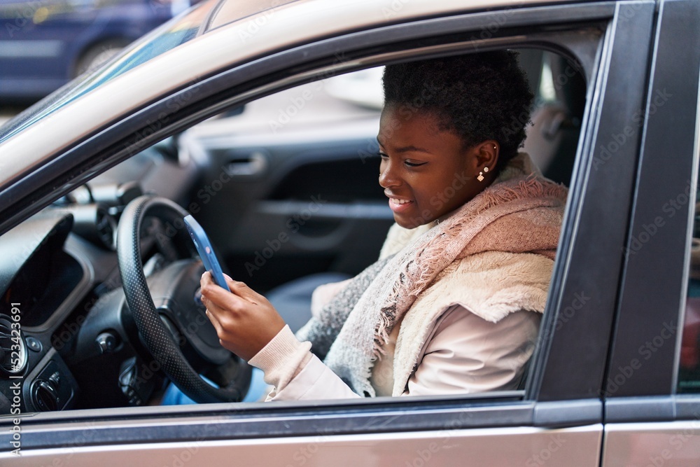 African american woman using smartphone sitting on car at street