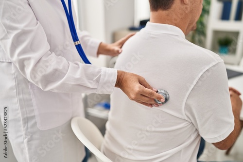 Middle age man and woman doctor and patient auscultating pulmonary sound having medical consultation at clinic