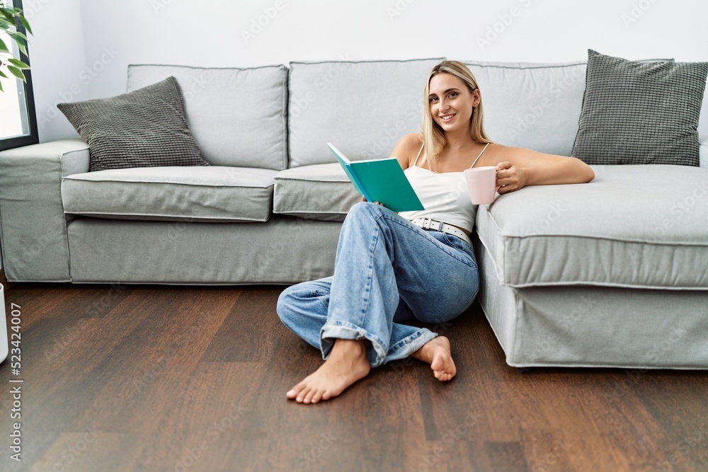 Obraz premium Young blonde woman reading book drinking coffee at home