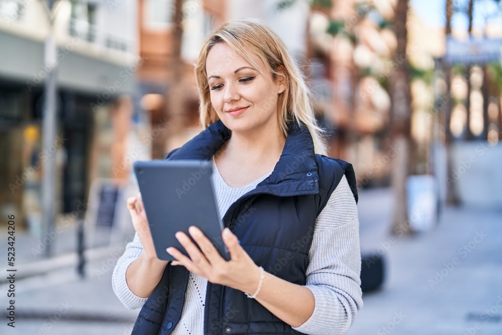 Young blonde woman smiling confident using touchpad at street